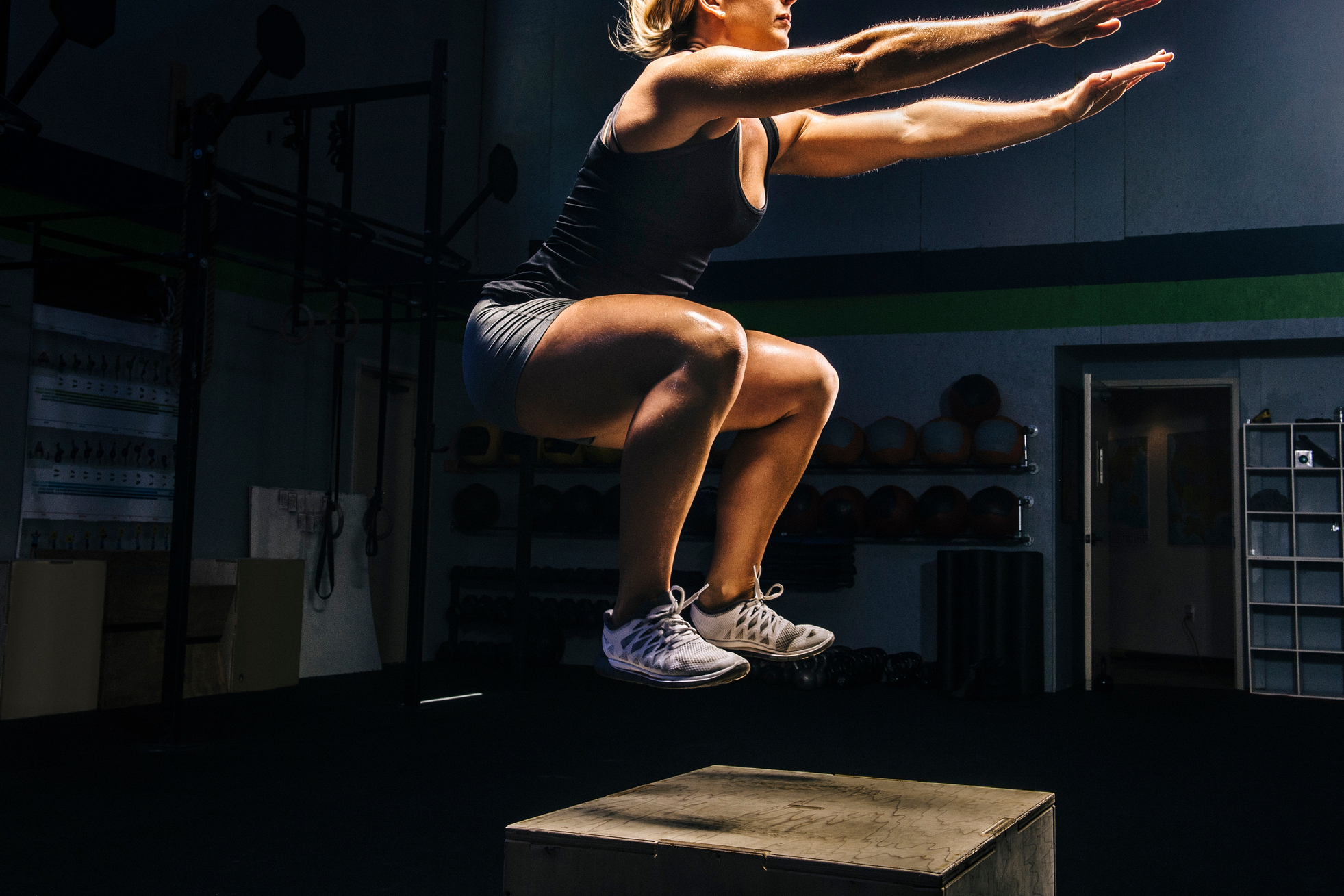 Young woman jumping mid air on gym box with arms reaching out